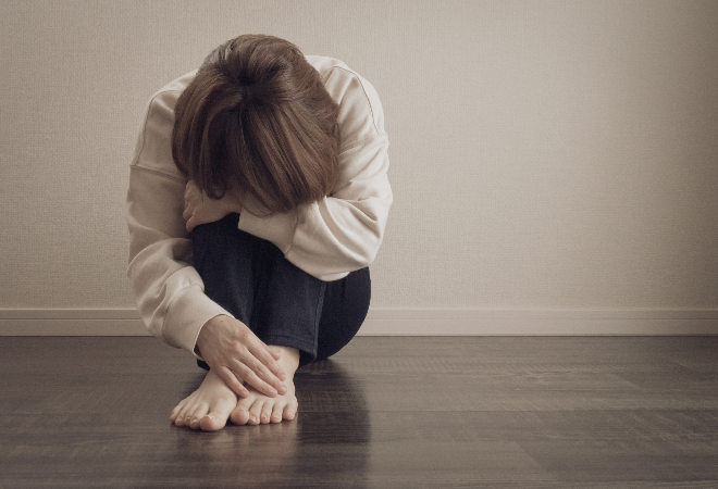膝を抱えうずくまる女性の画像。