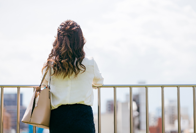 屋上で外を眺める女性社員の後ろ姿。